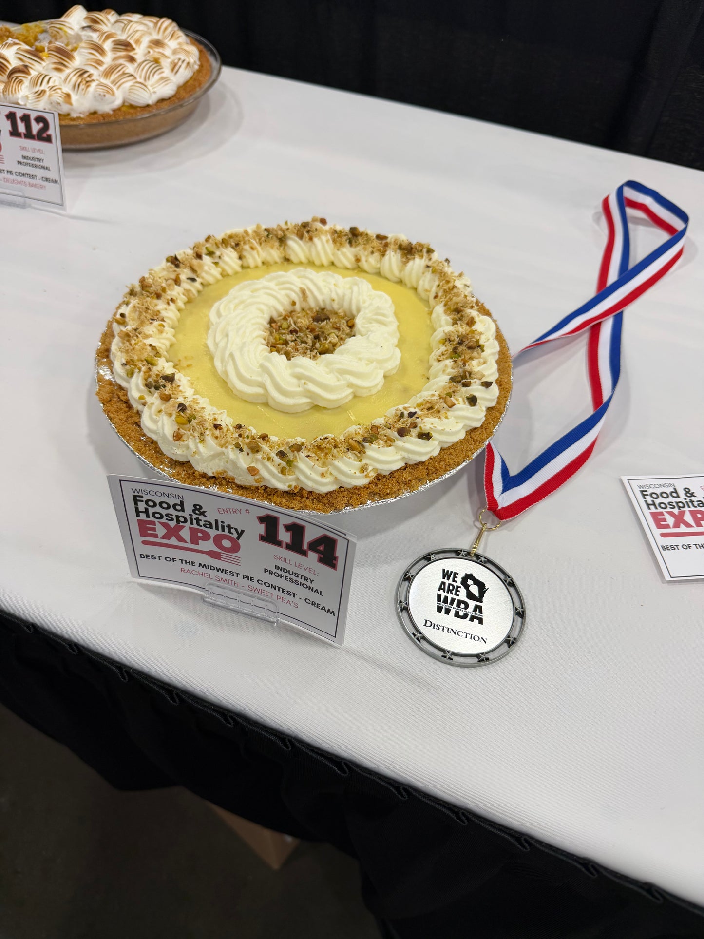 a banana cream pie decorated with whipped cream and chopped dried banana chips with a second place award from the wisconsin bakers association 2026 cream pie competition